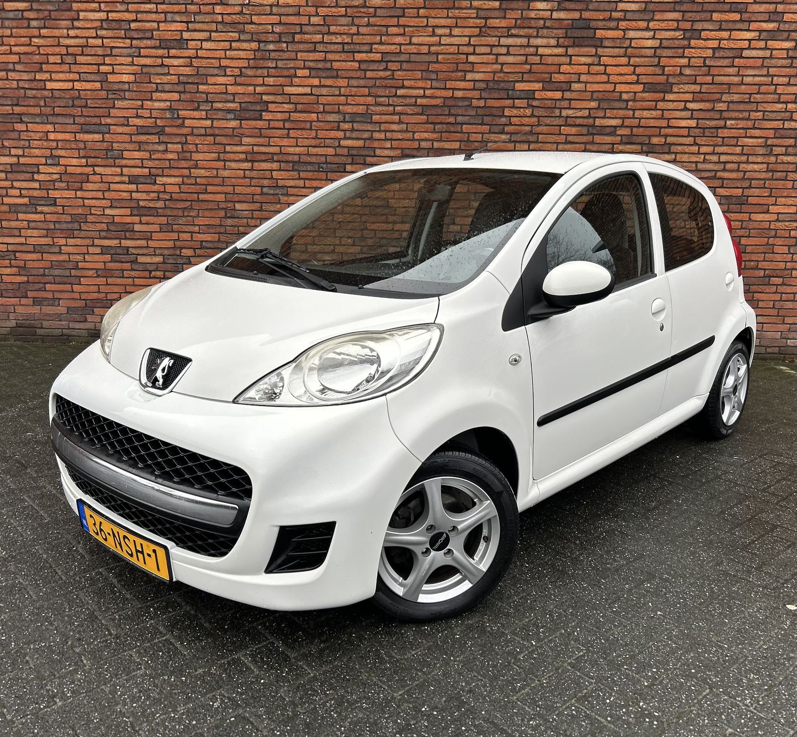 Witte Peugeot 107 voor de bakstenen muur bij Faber auto's