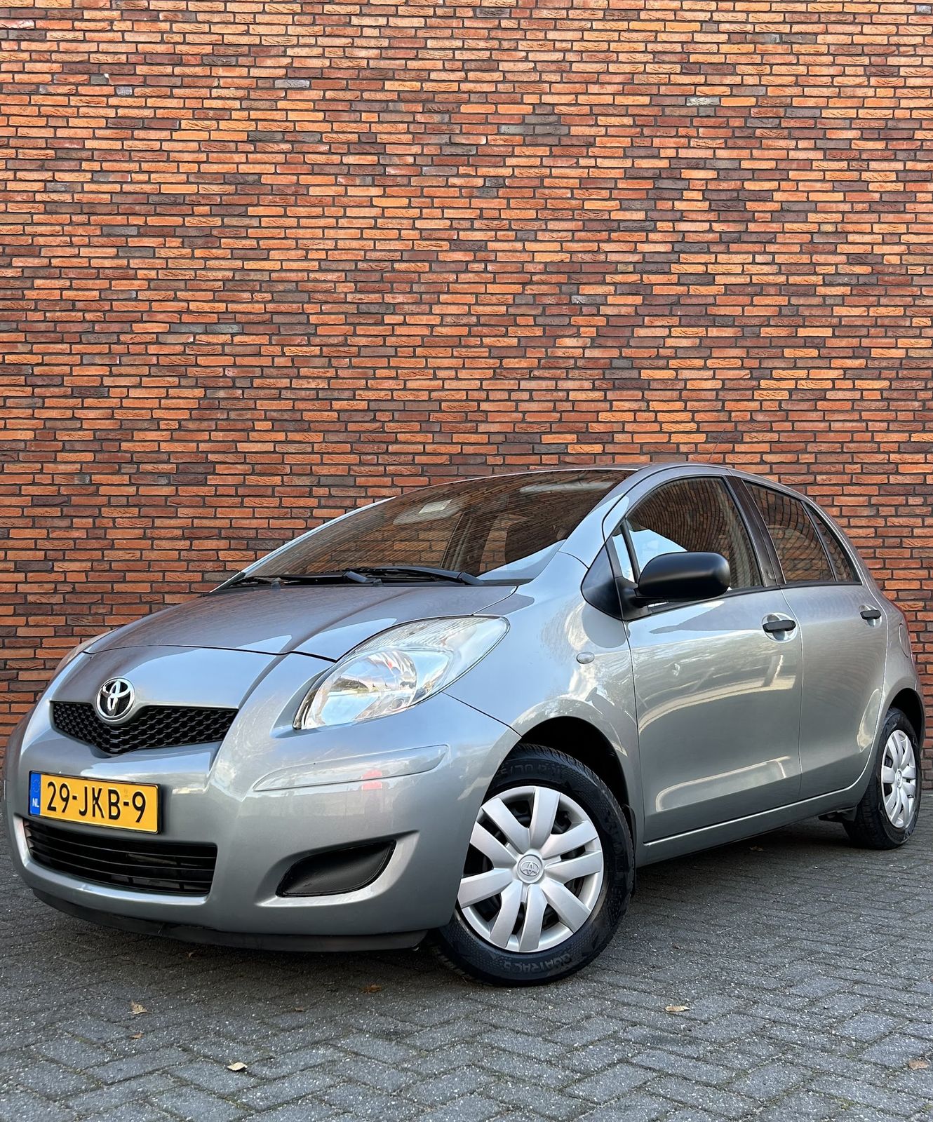 Zilvergrijze Toyota Yaris, glanzend gepoetst, voor de bakstenen muur