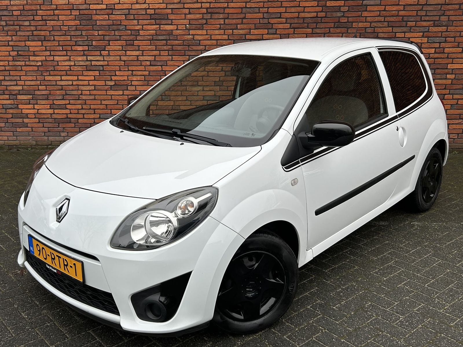 Witte Renault Twingo met zwarte velgen voor de bakstenen muur